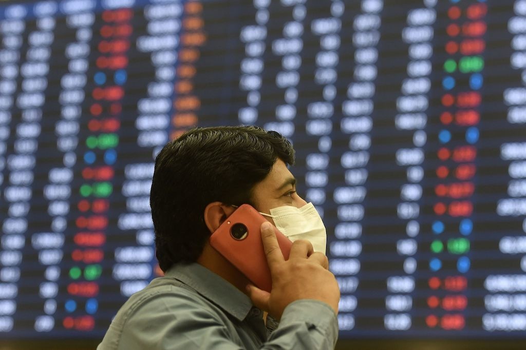 A stockbroker wearing a mask speaks on his cellphone as he watches share prices on a screen at the Pakistan Stock Exchange in Karachi | Asif Hassan, AFP